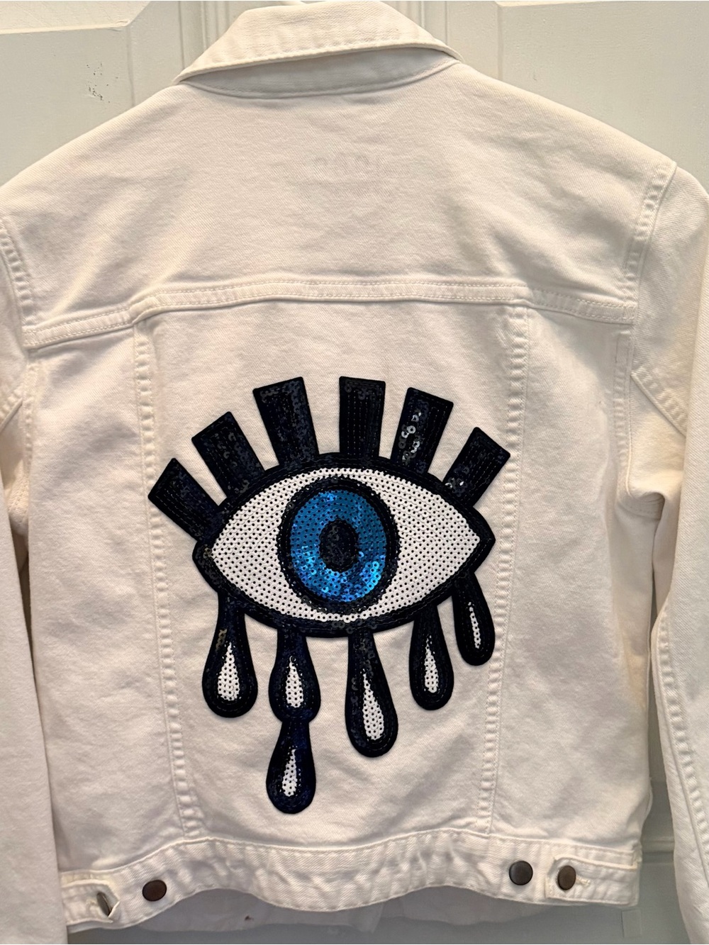 White Denim Jacket with Blue Sequin Evil Eye Graphic by Gap.
